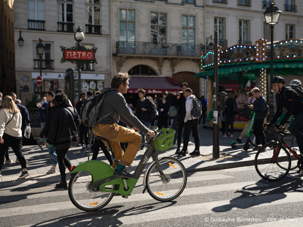 Cyclist riding a green Velib bike on a pedestrian crossing in Paris.